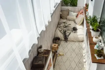 Przytulny balkon w stylu boho: łóżko z kocem, poduszki, dywan, rośliny i drewniane dekoracje. Idealne inspiracje na relaks.